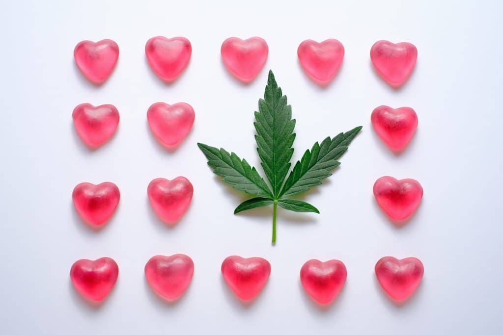 pink heart-shaped gummies lined up around a marijuana leaf